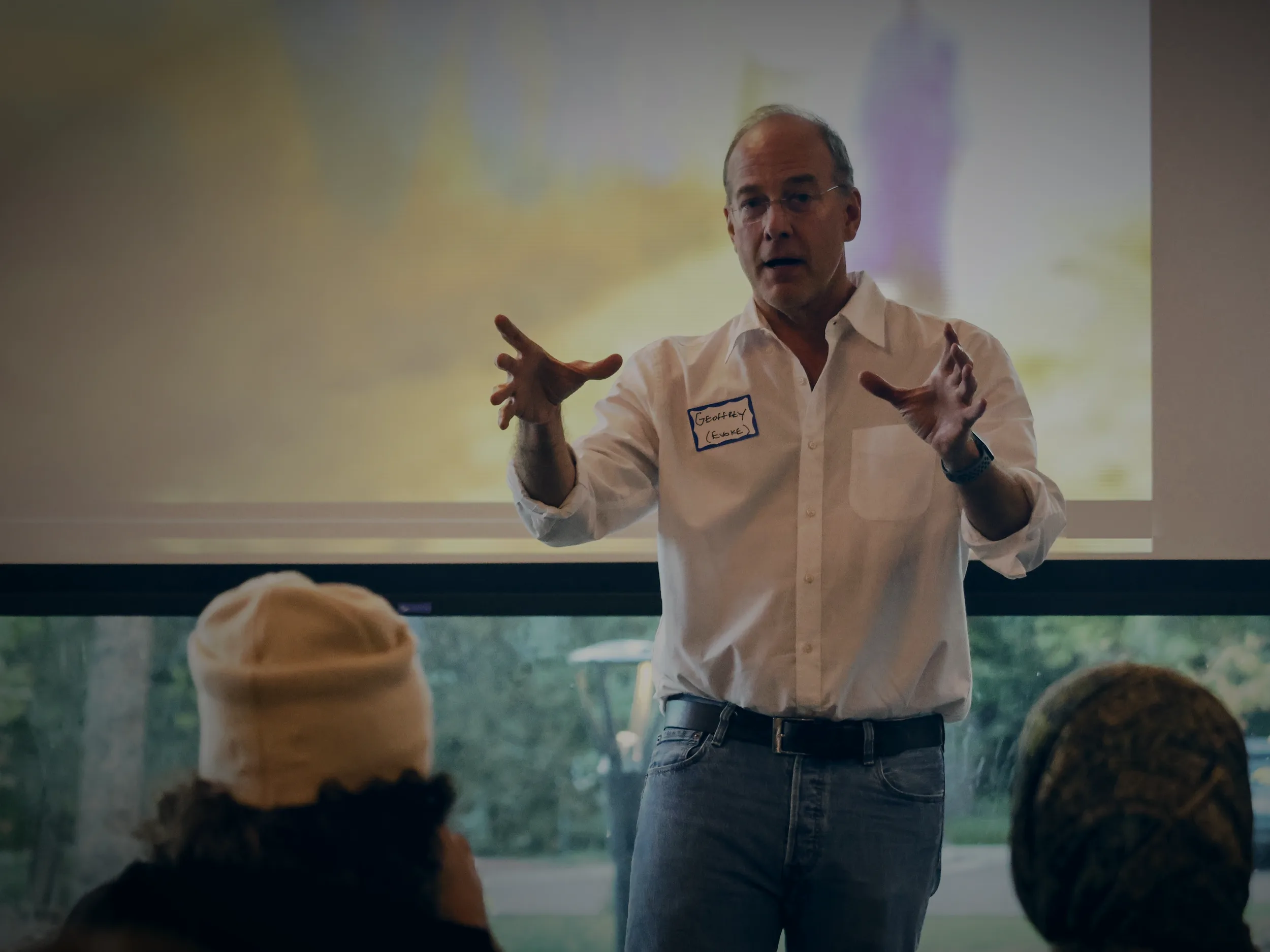 Geoffrey Kirkman speaking to a room of young people at an EVOKE design sprint in Boulder, a projected image on the screen behind him